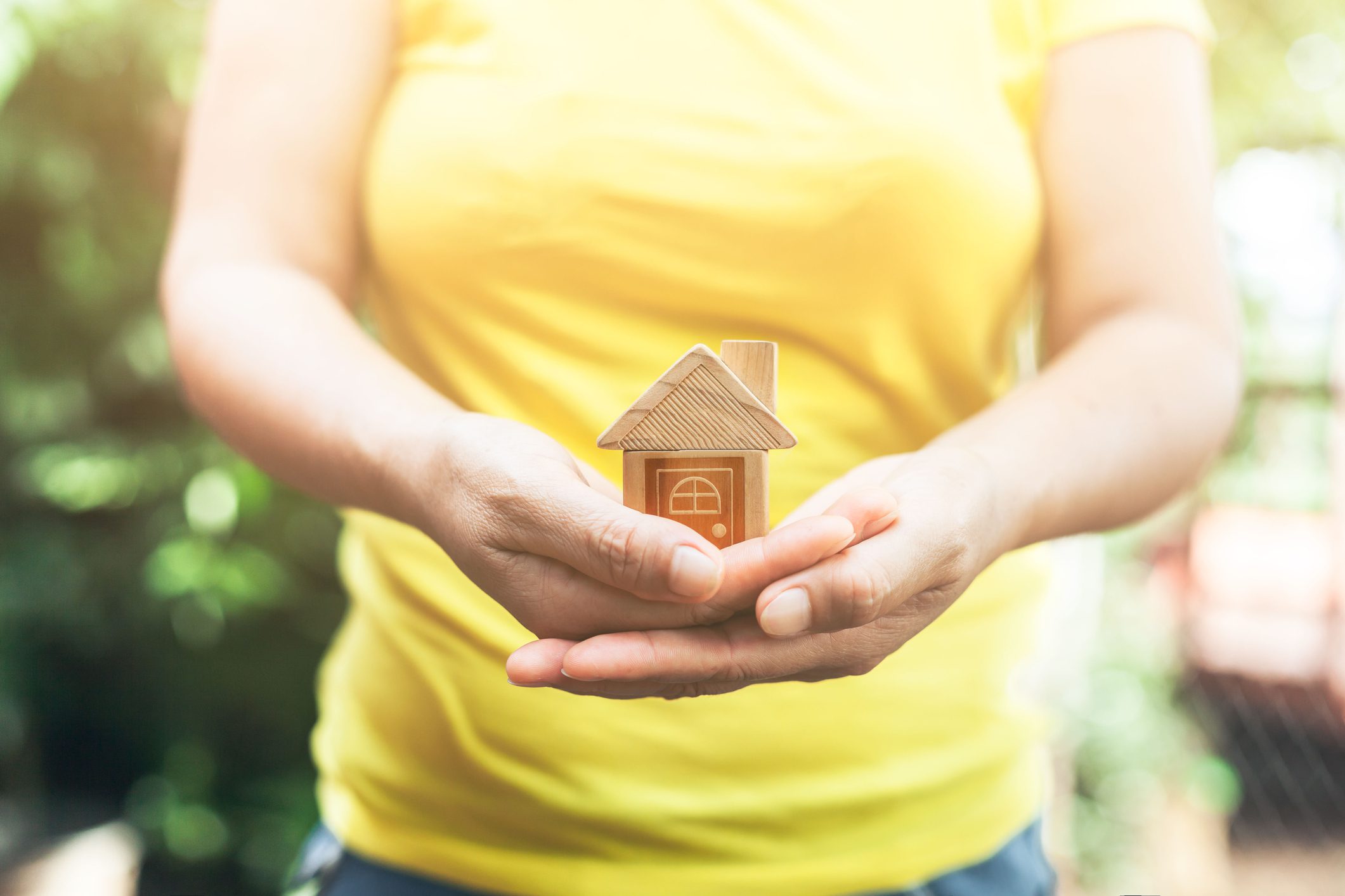 Hands holding small wooden house model.