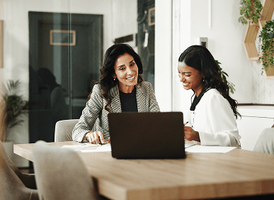 Two women smiling at office desk.