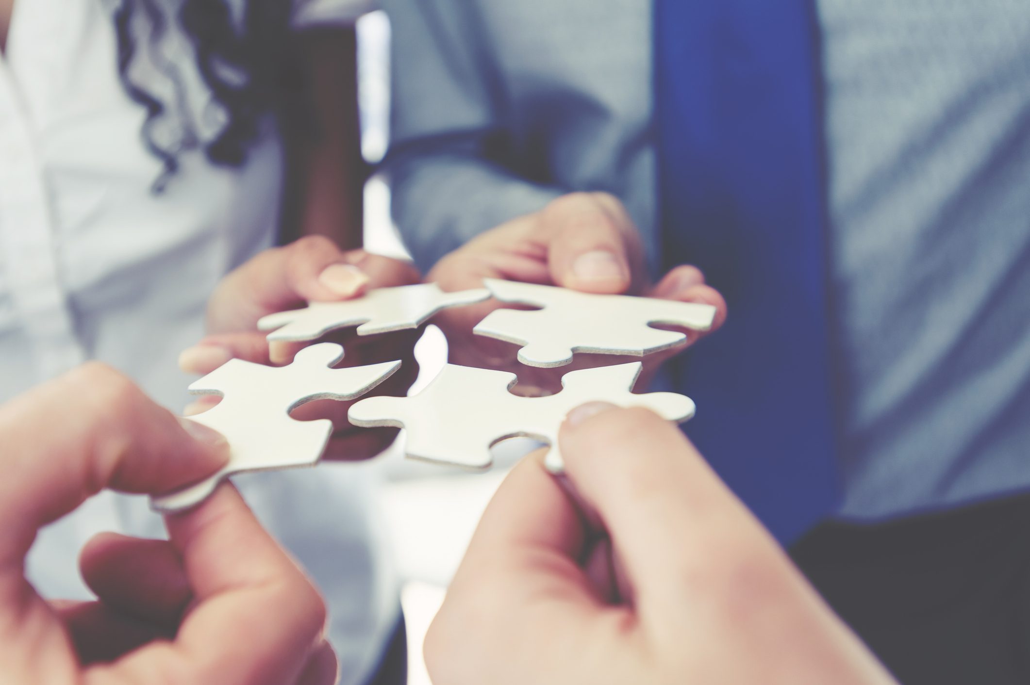 Hands connecting puzzle pieces in collaboration.