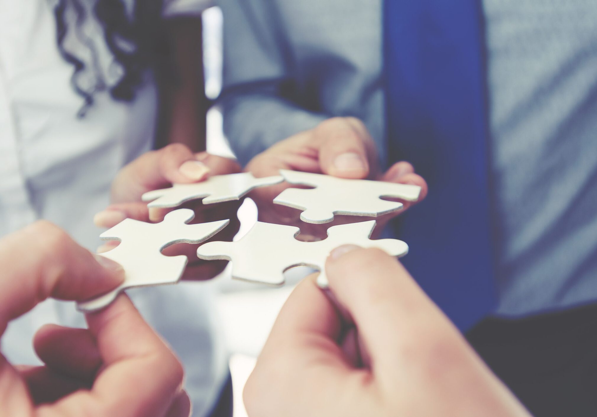 Hands connecting puzzle pieces in collaboration.